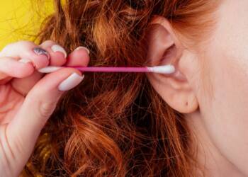 curly redhead caucasian woman use ears sticks in studio yellow background.