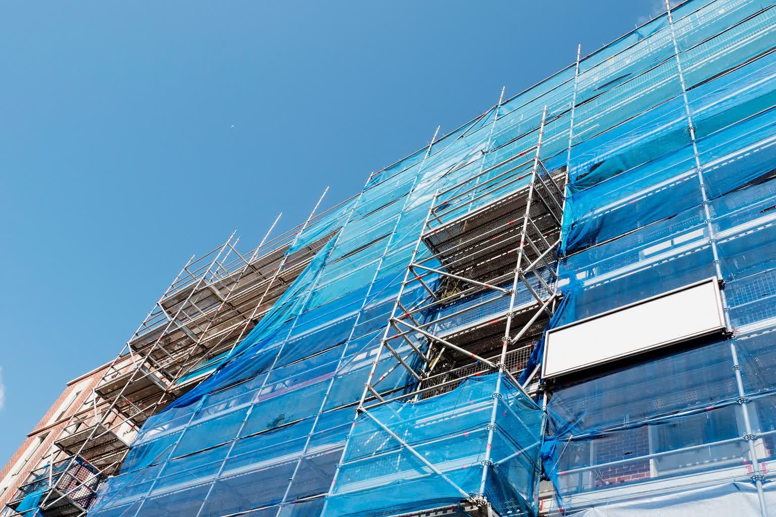 Siatki BHP – rodzaje, zastosowania, przepisy 2 Zbliżenie na niebieską siatkę zamontowaną na rusztowaniu przy budynku - sklep.symar.pl