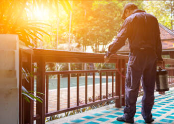 exterminate termite control company employee is using a termite sprayer at customer's house and searching for termite nests to eliminate. exterminate control worker spraying chemical insect repellant